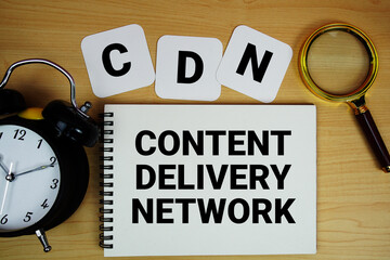 CDN Content Delivery Network text written on notepad with magnifying glass and alarm clock on wooden background © may1985