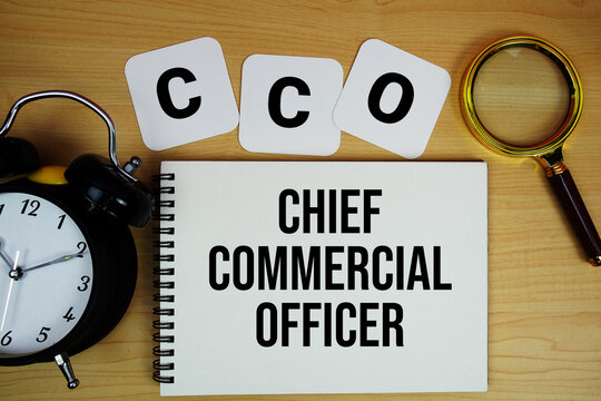 CCO Chief Commercial Officer text written on notepad with magnifying glass and alarm clock on wooden background