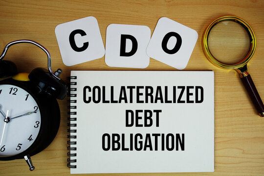 CDO Collateralized Debt Obligation text written on notepad with magnifying glass and alarm clock on wooden background