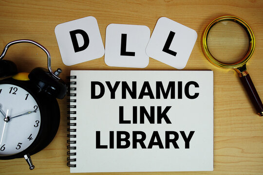 DLL Dynamic Link Library text written on notepad with magnifying glass and alarm clock on wooden background