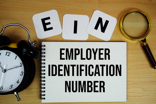 EIN Employer Identification Number text written on notepad with magnifying glass and alarm clock on wooden background