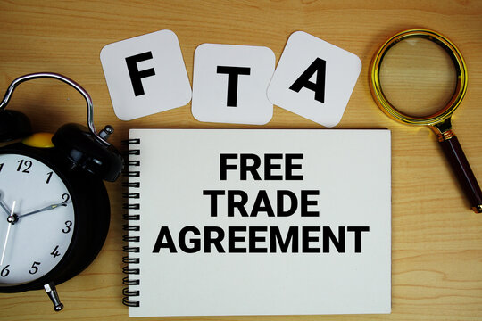 FTA Free Trade Agreement text written on notepad with magnifying glass and alarm clock on wooden background