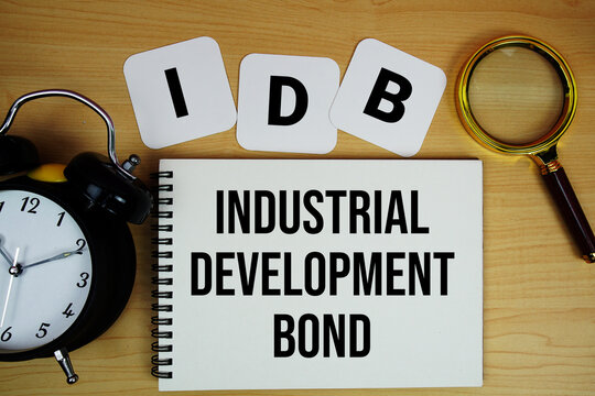 IDB Industrial Development Bond text written on notepad with magnifying glass and alarm clock on wooden background