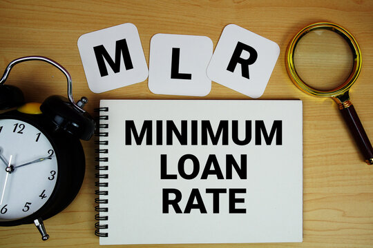MLR Minimum Loan Rate text written on notepad with magnifying glass and alarm clock on wooden background