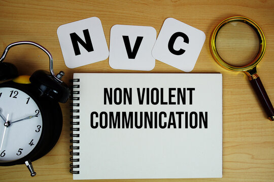 NVC Non Violent Communication text written on notepad with magnifying glass and alarm clock on wooden background