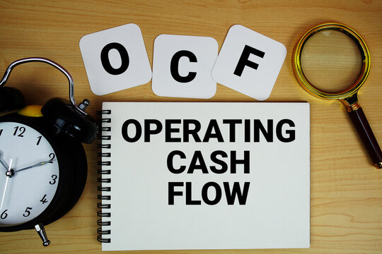 OCF Operating Cash Flow text written on notepad with magnifying glass and alarm clock on wooden background