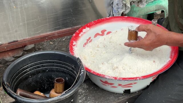 An Asian man selling traditional food fills a bamboo mold with Putu cake batter made from rice flour and palm sugar before the steaming process begins.