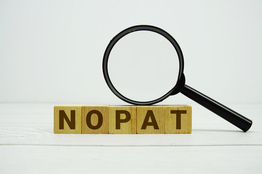 NOPAT (Net Operating Profit After Tax) alphabet letters with magnifying glass on wooden background