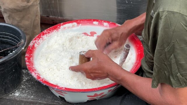 An Asian man selling traditional food fills a bamboo mold with Putu cake batter made from rice flour and palm sugar before the steaming process begins.