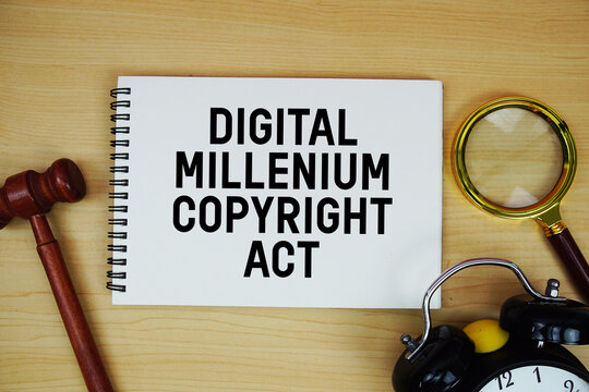 DMCA Digital Millennium Copyright Act text written on notepad with pen, alarm clock and judge gavel on wooden background