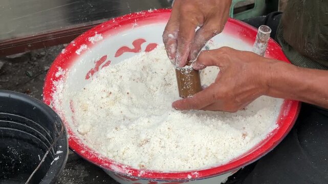An Asian man selling traditional food fills a bamboo mold with Putu cake batter made from rice flour and palm sugar before the steaming process begins.