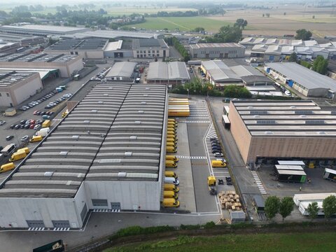 Industrial Park Panorama: An aerial view showcases a sprawling industrial park, featuring large warehouses, loading docks, and a fleet of yellow trucks ready for distribution.