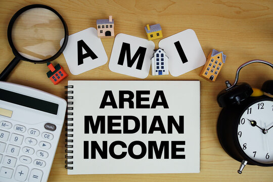 AMI Area Median Income text written on notepad with house model, alarm clock and magnifying glass on wooden background