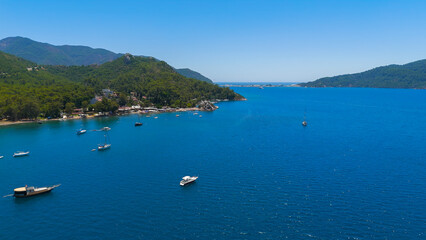 Fototapeta premium Marmaris, Turkey. Aerial drone flight along lush green forest coastline in Marmaris Bay. Sandy beaches, yachts sailing on blue water and coastal road on a sunny day.. Aerial View