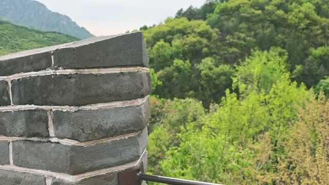 Great Wall China. Stone wall corner of ancient structure with metal railing overlooking lush green hillside and distant watchtower in the background