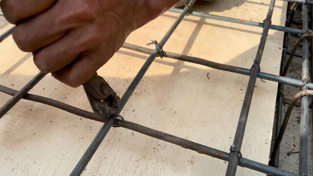 Construction worker tying steel rebar with wire and pliers for concrete reinforcement