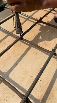 Construction worker using pliers to tie steel rebar grid on wooden formwork