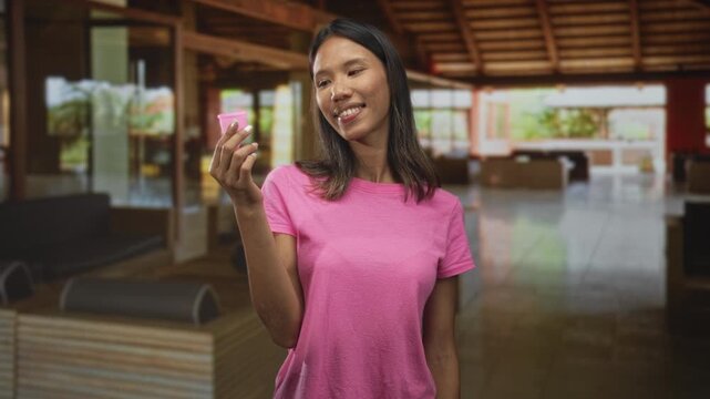 Woman holding pink menstrual cup in hand inside a building, smiling while inspecting the product; confidence wellness.