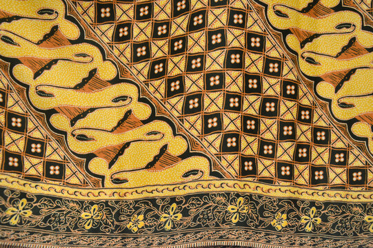Traditional Indonesian batik fabric featuring yellow parang patterns and brown geometric diamond motifs. Ethnic textile background for fashion and interior decor.
