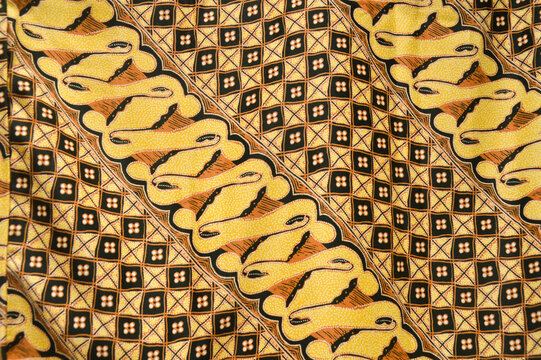 Traditional Indonesian batik fabric featuring yellow parang patterns and brown geometric diamond motifs. Ethnic textile background for fashion and interior decor.
