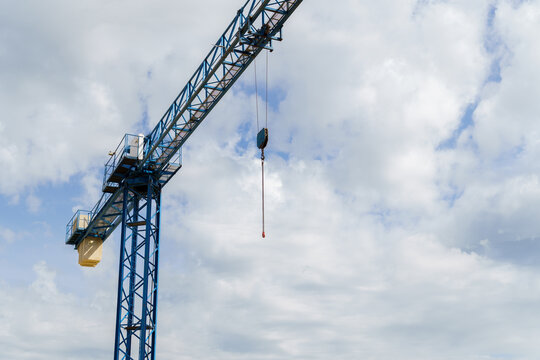 Blue construction crane hook and jib against a cloudy sky, representing engineering, heavy lifting, and urban development