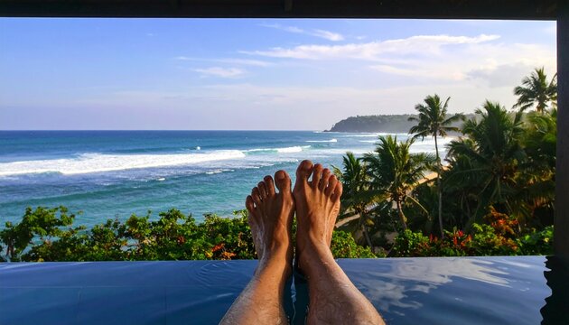 Feet relaxing at infinity pool overlooking tropical ocean shoreline