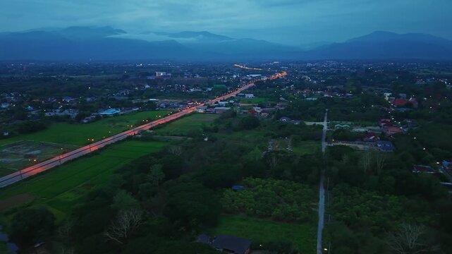 Cinematic aerial reveal from nadir to horizon over a central highway Features vehicles moving through green farming zones toward a wide skyline in a quiet and evolving eastern regional district