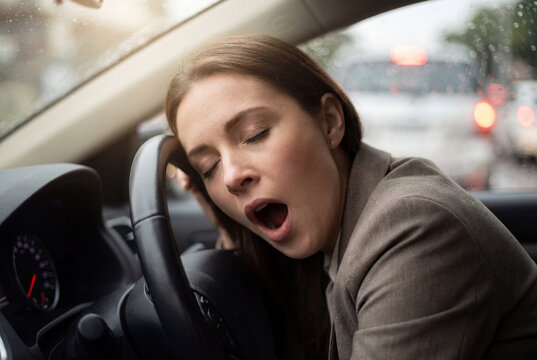 Sleepy woman yawning while driving her car, showing signs of dangerous fatigue