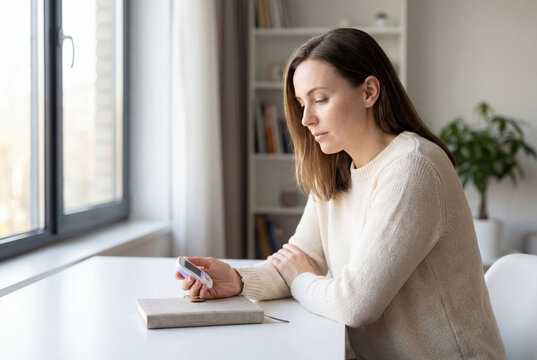 Downcast woman holds digital fertility tracker and personal planner
