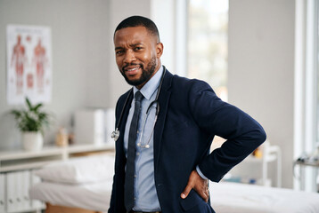 Fototapeta premium African american doctor touching lower back while experiencing pain in medical clinic