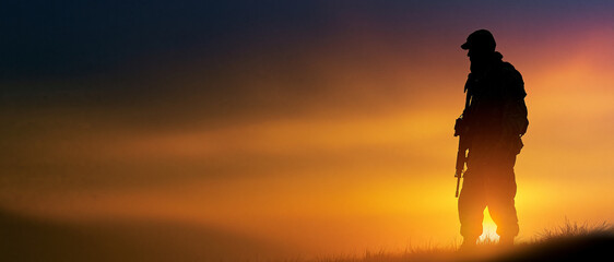 Naklejka premium Soldier standing in silhouette against a dramatic sunset background - 