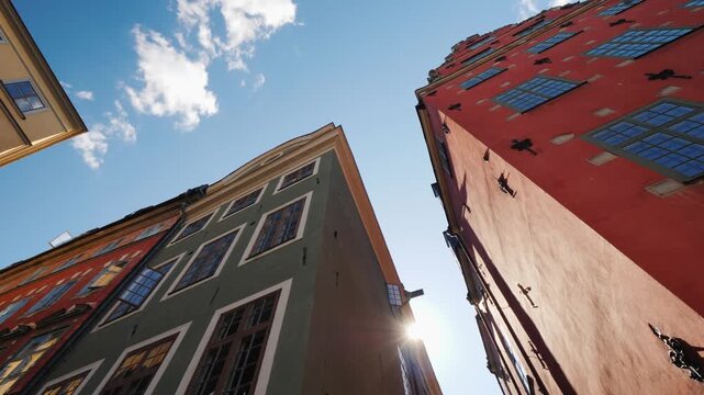 Stockholm old town architecture with colorful facades in gamla stan at sunset as camera moves along narrow streets revealing sun flare between medieval historical buildings and blue sky with clouds.