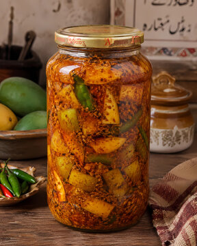 Traditional Pakistani homemade spicy mango and green chili pickle in a glass jar on a wooden table