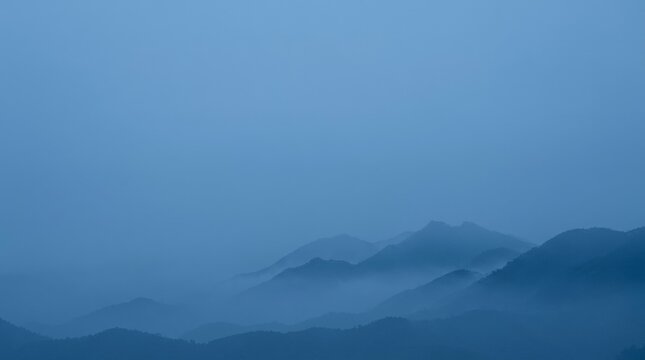 Serene blue mountain ranges shrouded in mist, creating a layered, ethereal landscape.