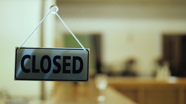 Hand flipping open to closed sign on glass door indicating business closure at evening time showing transition from daytime light to dark background in cinematic footage for retail store