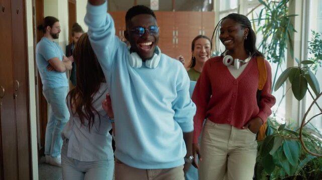 Slow motion of joyful university students laughing, dancing and joking while walking through campus hallway. Fun youth atmosphere and carefree student lifestyle.