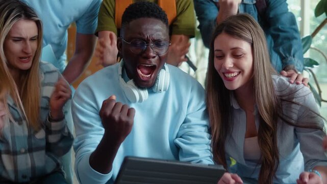 Excited university multiracial students celebrating victory while watching live content on tablet in campus hallway. Happy group reaction, teamwork and youth lifestyle.
