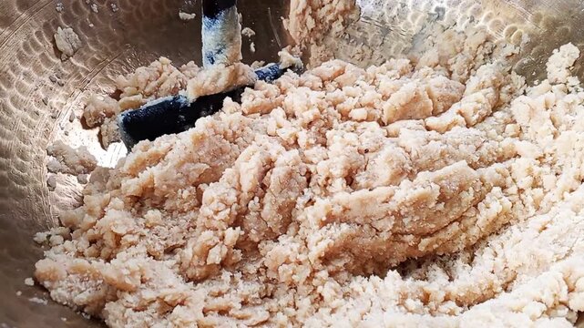 A metal spatula mixes raw cookie dough inside of a large hammered brass bowl to prepare for baking delicious homemade treats in a home kitchen