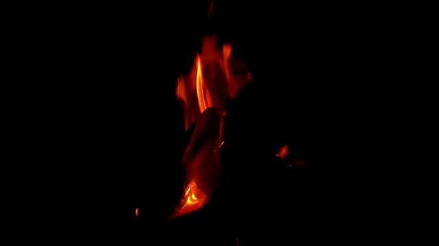 Bright orange flames flicker and dance intensely above a burning wooden log isolated against a completely dark black background providing a dramatic and warm visual experience