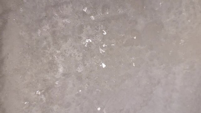 Detailed close up view of white bubbly foam texture showing many small air bubbles creating a soft organic pattern on a smooth light gray surface area