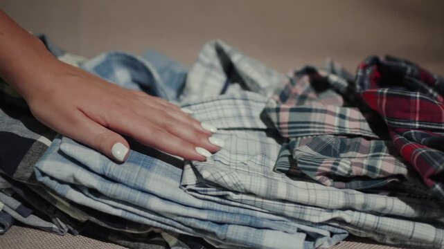 A motion of female hand caressing neatly folded piles of plaid flannel shirts arranged by color from red to blue, showcasing a variety of patterns and textures perfect