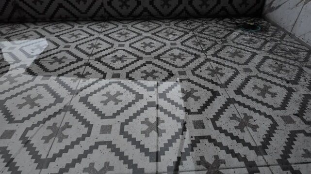 High-angle shot of standing water reflecting light on a black and white geometric patterned floor, showing a drainage issue in a residential area.