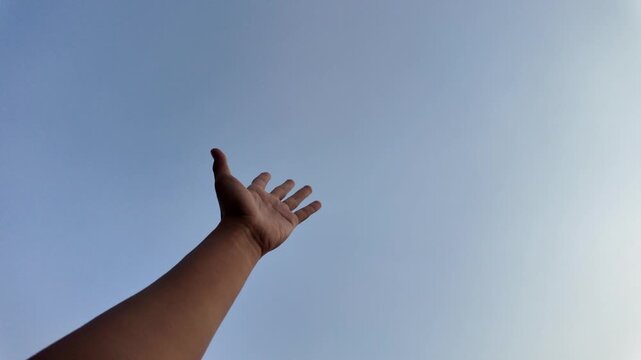 A close-up shot of a male left hand waving side to side against a vast, bright blue sky background. This gesture represents a friendly greeting, a warm welcome.