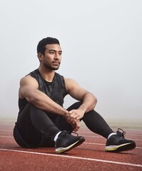 Obraz premium Thinking, track and man on floor with race or training idea for sports in mist or fog. Confident, fitness and athlete or runner for competition, tournament and wellness strategy for outdoor workout