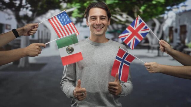 Man smiling with thumbs up as hands hold and wave usa uk mexico norway flags on a street; multicultural celebration joy.