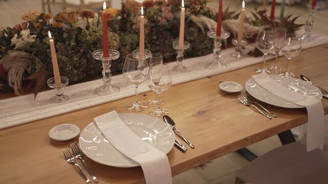 Dining table arranged with plates glasses candles and flowers for event setting