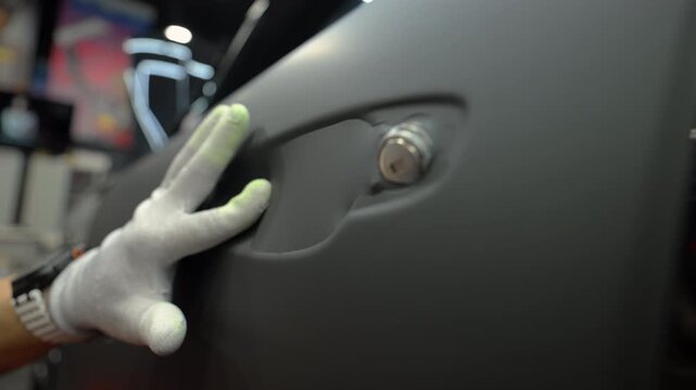 Close up of a worker applying matte vinyl wrap on a car body panel in a workshop. Automotive detailing process with protective film installation, smooth matte finish and precision work.