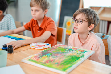 Fototapeta premium Back to school and education concept of children painting classroom art lesson creative activity, boy and girl at table with canvas and paint in bright classroom