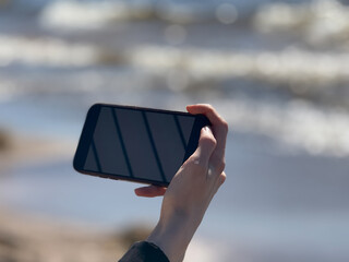 Hand Holding Smartphone by Sea with Blurred Ocean Background © Emils