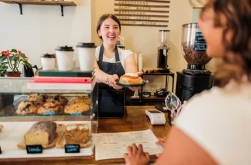 Fotobehang Horeca Happy barista serving delicious cinnamon roll to customer  © PintoArt